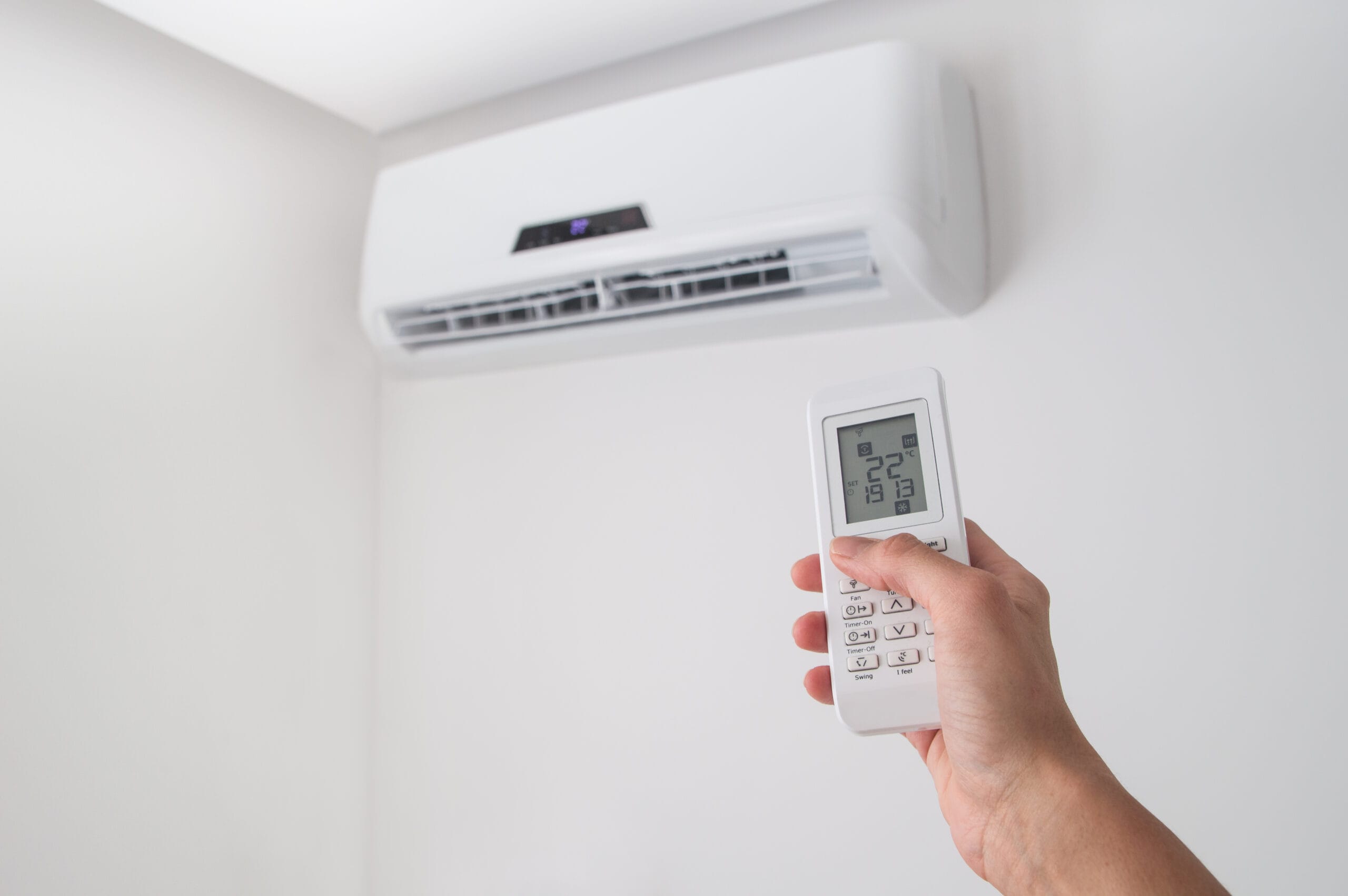 hand,holding,remote,control,,adjusting,temperature,of,air,conditioner,mounted