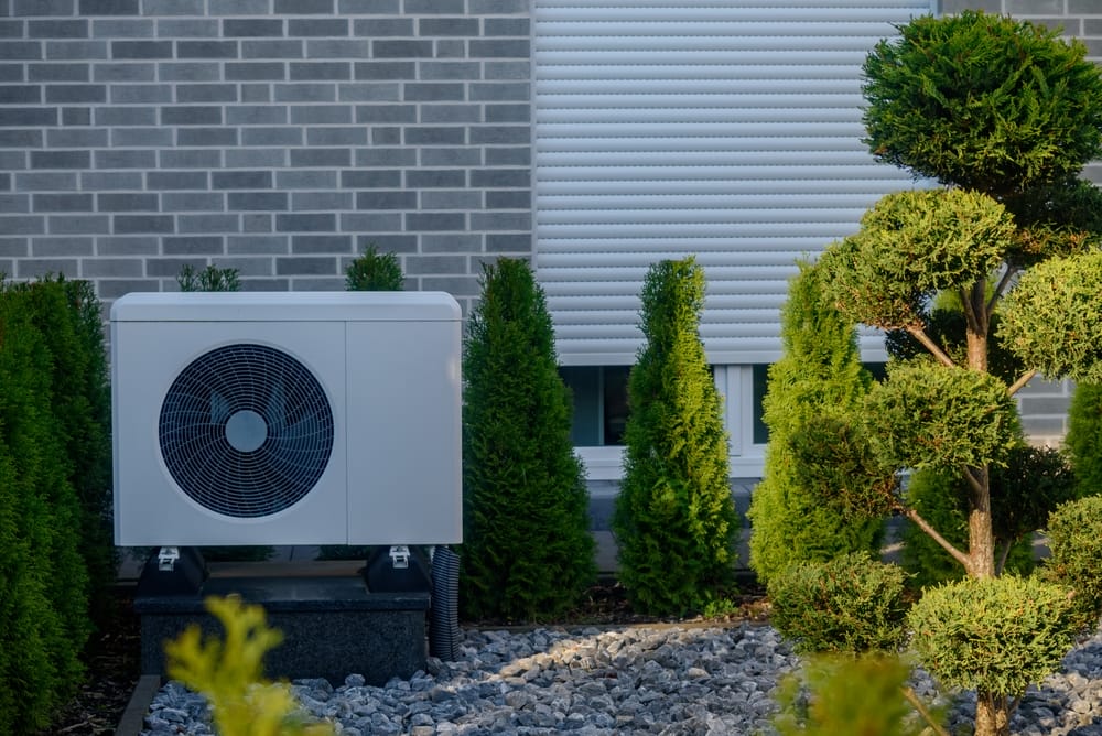 unité de pompe à chaleur extérieure installée dans un jardin bien entretenu aux arbustes taillés