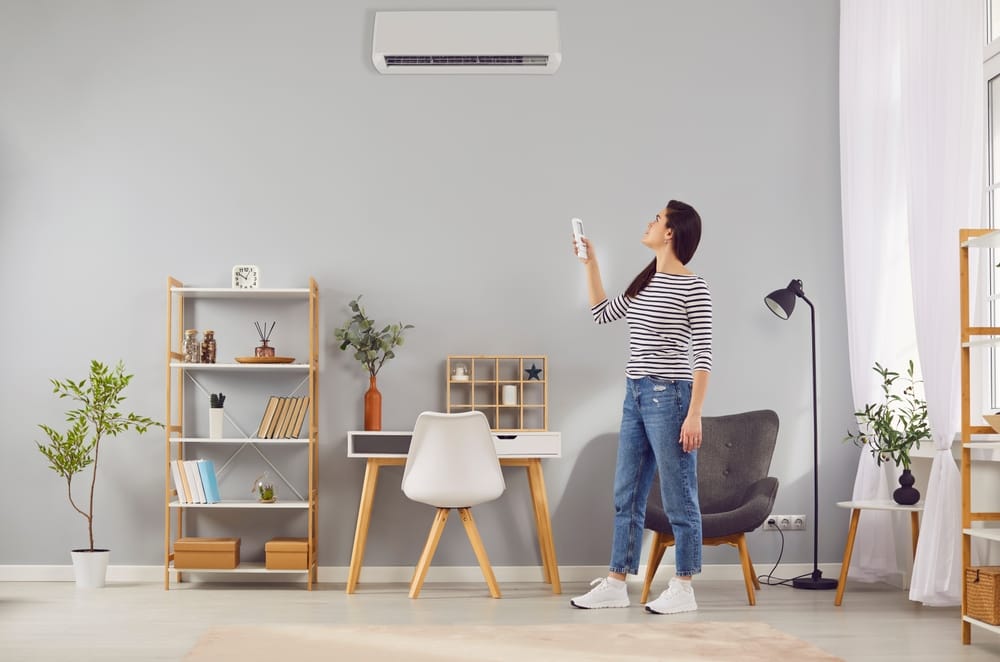 Locataire ou propriétaire d’appartement allumant un système de climatisation moderne à la maison. Jeune femme debout dans un beau salon réglant la température sur un climatiseur fixé à un mur gris. Concept de climatisation.