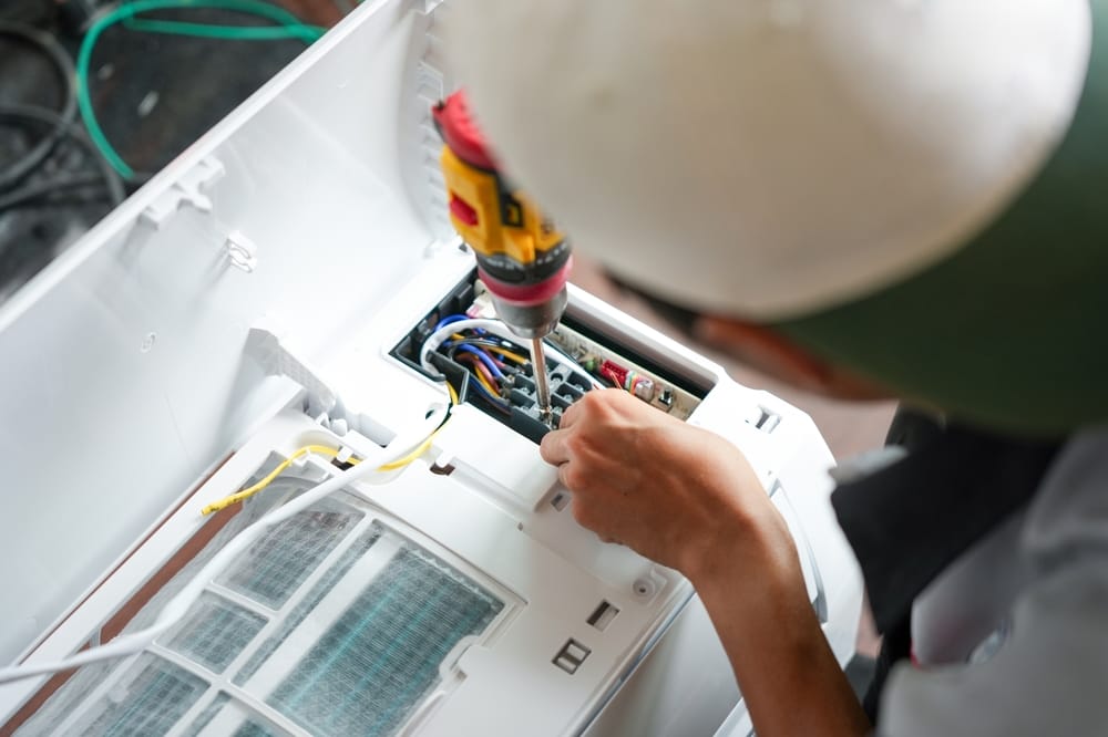 Homme utilisant un tournevis pour réparer un climatiseur, gros plan sur un réparateur de climatisation travaillant sur les composants internes, technicien installant une unité de climatisation intérieure.