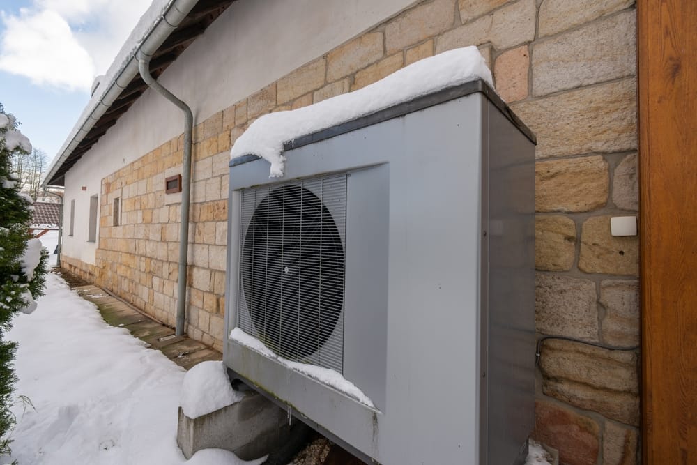 Air heat pump beside house in winter, against sandstone wall